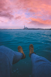 Low section of person over sea during sunset