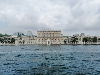 Buildings by sea against cloudy sky