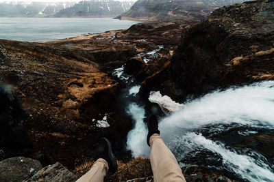 Low section of person sitting by waterfall