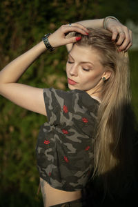 Side view of young woman with hand in hair standing on field