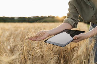Woman holding digital tablet in field examining barley ear