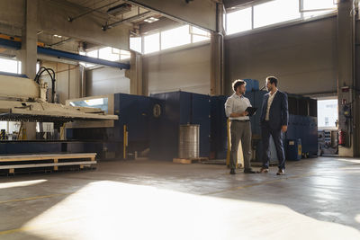 Businessman and colleague with digital tablet working while standing at factory