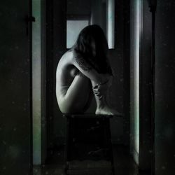 Side view of naked woman sitting in darkroom