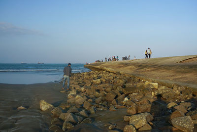 People on rocks by sea against sky