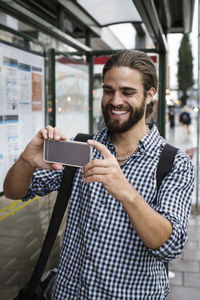 Man taking photograph with smartphone at bus stop