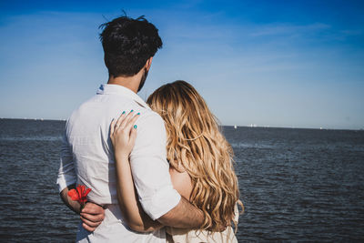 Rear view of couple embracing at beach against sky