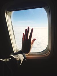Cropped image of hand against sky seen through airplane window