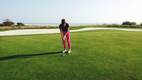 Full length of woman playing golf on field against clear sky