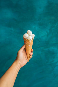 Close-up of hand holding ice cream cone against blue background