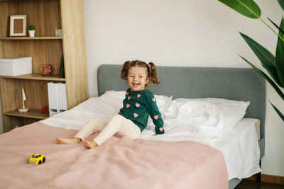 A charming little girl is playing with a car on the bed and fooling around
