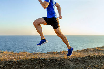 Man athlete runner running mountain trail in background of sea and sky