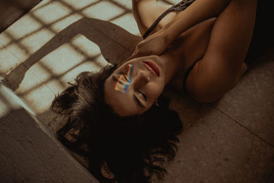 High angle of serene female with rainbow light on face lying on floor with closed eyes in room with sunlight