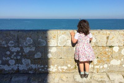 Full length rear view of girl standing by retaining wall against sea