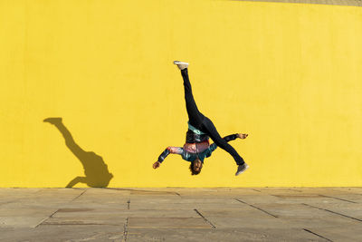 Acrobat jumping somersaults in front of yellow wall