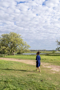 Rear view of woman walking on field against sky