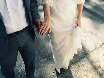 Low section of bride and groom holding hands while standing on street