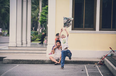 Boy playing with newspaper while father and daughter sitting outside house