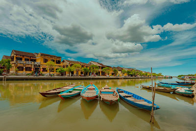 Boats moored in lake against cloudy sky