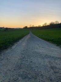 Empty road amidst field against sky during sunset