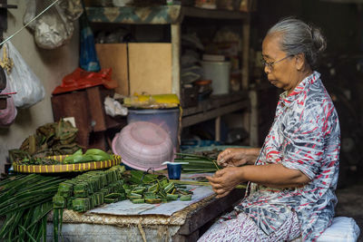 Side view of woman wrapping leaves on table