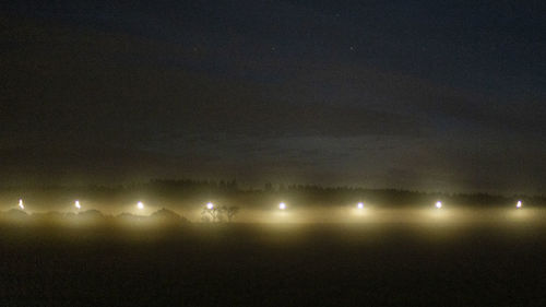 Illuminated light trails on landscape against sky at night