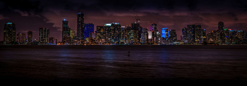 Illuminated cityscape against calm sea at night