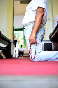 Low section of man holding prayer beads while kneeling at church