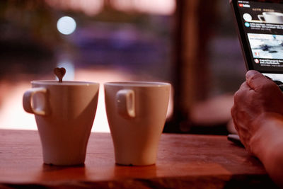 Close-up of hand holding coffee cup on table