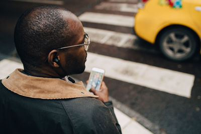 Rear view of businessman using mobile phone while crossing road in city