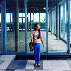 Full length of young woman standing against glass