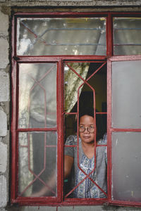 Portrait of young woman looking through window