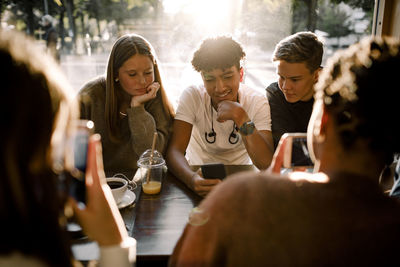 Teenage girls and boys using social media on smart phones while sitting in cafe