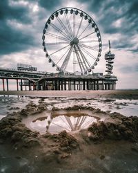 Ferris wheel by sea against cloudy sky