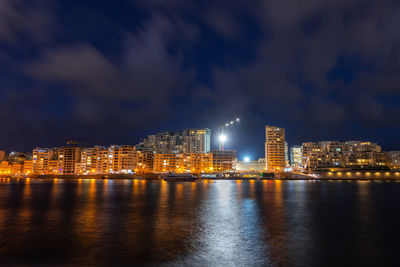 Illuminated city by river against sky at night