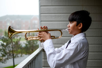 Side view of boy playing musical instrument while standing by railing