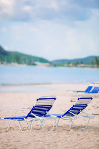 Deck chairs on beach against sky