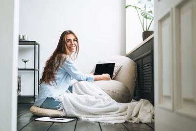 Young smiling woman in blue shirt using laptop in room