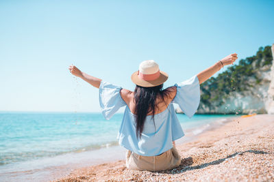 Rear view of woman with umbrella at beach against clear sky