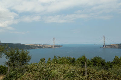 Suspension bridge over river against cloudy sky