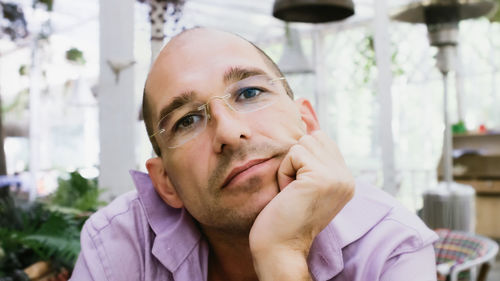 Attractive bald man wearing glasses sits on the summer terrace in a pensive mood. soft focus.