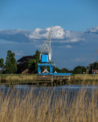 Traditional windmill on field by lake against sky