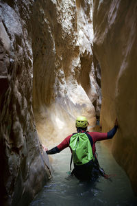 Rear view of hiker with backpack wading amidst canyon while canyoneering