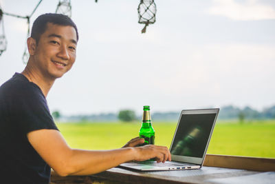 Portrait of man using laptop by field