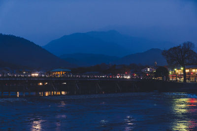 Illuminated city by mountains against sky at night