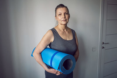 Woman aged athlete stands in a white room with a yoga mat