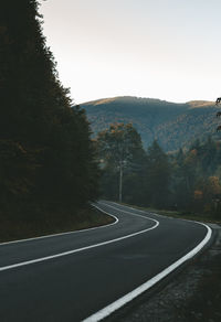 Country road by trees against clear sky