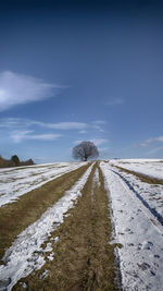 Tire tracks on snow field against sky