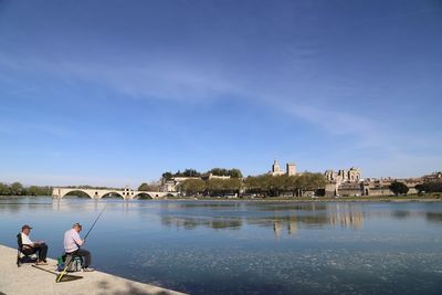 People sitting on river by city against sky