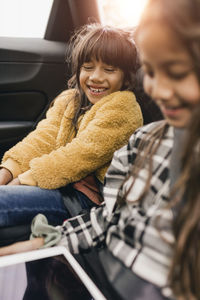 Smiling sisters using digital tablet while traveling in electric car