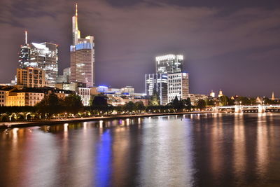 Illuminated buildings by river against sky in city at night